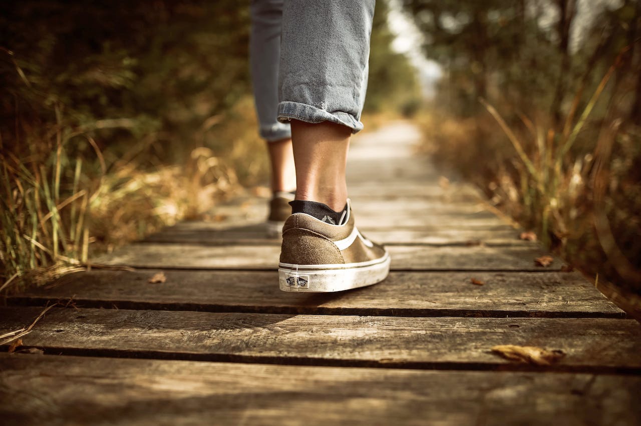 Person in Sneaker, die auf einem Holzweg in Natur spazieren geht